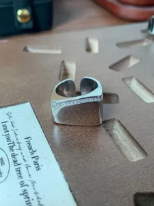 Dettaglio dell'anello aperto in metallo largo con una fila di zirconi luminosi e finitura liscia.