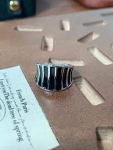 Primo piano dell'ampio anello aperto in metallo rigato con finitura in smalto nero e dettagli.