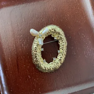 Gros plan détaillé d'une broche en métal doré irrégulier ornée de perles d'eau douce et de cristaux.