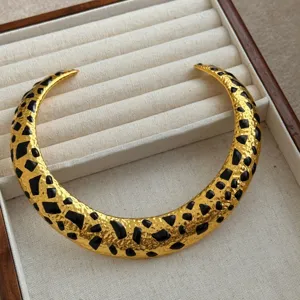 Primer plano del collar gargantilla dorado con incrustaciones geométricas de esmalte negro.