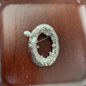 Gros plan détaillé de la broche lettre en métal et perles d'eau douce avec texture martelée.