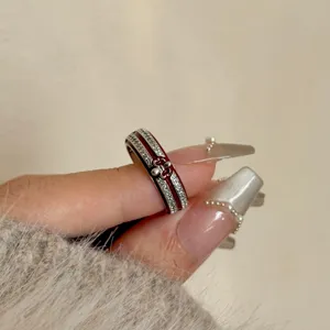 Primo piano dettaglio di un anello regolabile impilabile con croce in smalto rosso e strass al dito.