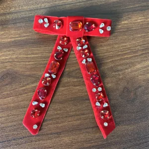 Dettaglio spilla fiocco in velluto strass rosso, decorazione cristallo scintillante, accessorio chic.