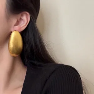 Gros plan de boucles d'oreilles ovales dorées surdimensionnées, bijoux statement minimalistes.