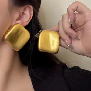 Boucles d'oreilles carrées dorées et massives, gros plan détaillé sur la texture brillante.