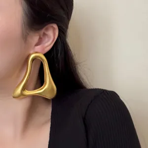 Gros plan d'une boucle d'oreille géométrique dorée irrégulière portée avec texture fondue.