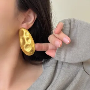 Gros plan de grandes boucles d'oreilles ovales dorées irrégulières au design texturé chic.