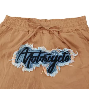 Close up of men's casual pants waist with drawstring and embroidered denim patch detail.
