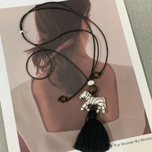 Detailed shot of a long sweater necklace featuring a silver zebra pendant and black tassel.