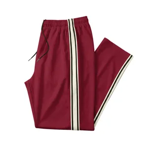 Détail pantalon de sport homme, rouge vin, coupe droite avec bande latérale contrastée.