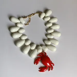 Gros plan détaillé du collier de perles blanches en forme de larme et pendentif crabe.