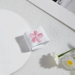 Nahaufnahme von weißem Stoff mit süßer rosa Kirschblütenstickerei, feines Kleidungsdetail.