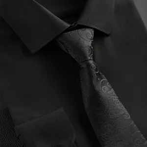 Close-up detail of black mens tie featuring vintage paisley pattern and shirt collar.
