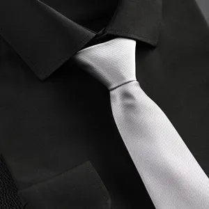 Detail view of a classic silver diagonal textured necktie paired with a black dress shirt.