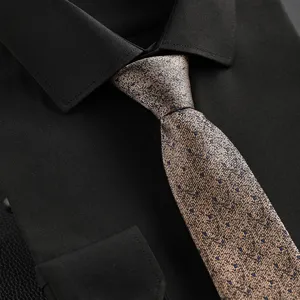 Detailed view of a champagne business necktie with subtle blue dots, paired with a black shirt.