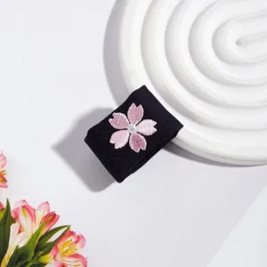 Detailansicht eines schwarzen JK-Uniform-Accessoires mit zarter rosa Kirschblüten-Bestickung.