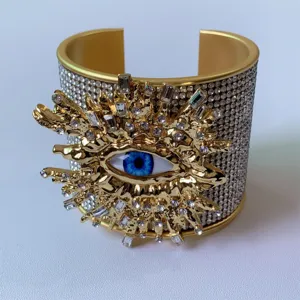 Primo piano dettagliato di un ampio bracciale rigido dorato con motivo malocchio e strass brillanti.