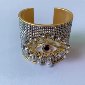 Bracciale rigido aperto placcato in oro con motivo malocchio in strass scintillanti e perle.