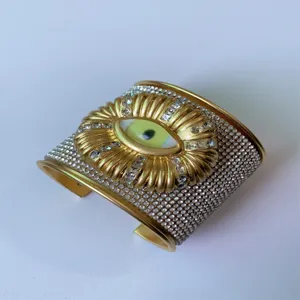 Vista dettagliata del bracciale rigido largo in metallo strass malocchio stile surrealista.