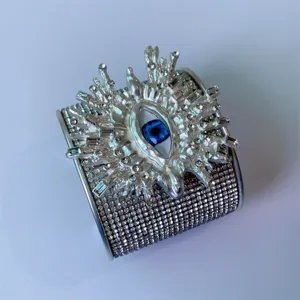 Vista dettagliata di un ampio bracciale rigido in metallo strass con motivo di occhio.