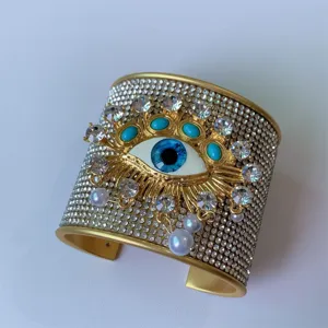Primo piano dettagliato del largo bracciale rigido dorato con occhio malvagio e strass.