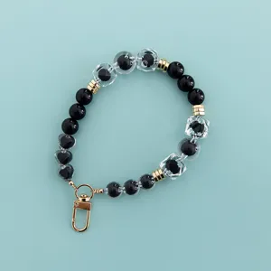 Close-up detail of black and clear crystal beaded phone charm strap with gold lobster clasp.