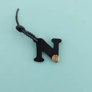 Gros plan du pendentif de sac en cuir PU noir lettre N avec bouton métallique et lanière.