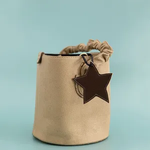 Beige leather bucket bag detail with stylish ruffled handle and elegant brown star charm pendant.