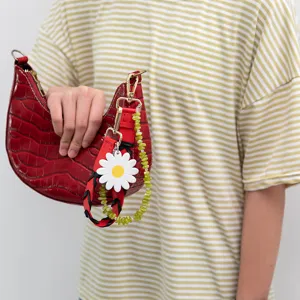 Close-up of stylish red crescent handbag featuring colorful straps, daisy charm and green beads.