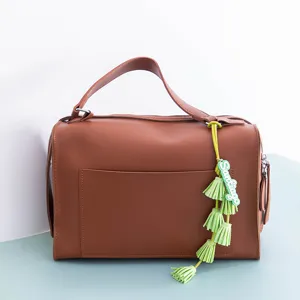 Brown PU leather handbag featuring a stylish light green tassel charm with custom text detail.