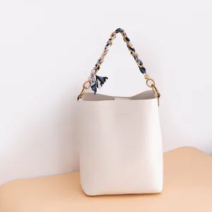 Bolso cubo de cuero blanco con cadena de metal y asa tejida de pañuelo de seda.
