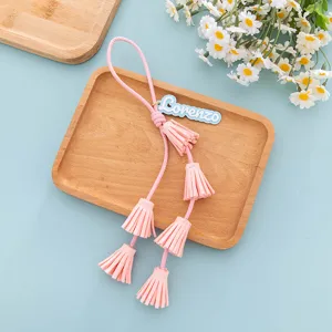 Pink PU leather tassel keychain bag charm detail shot with custom name tag and cute floral background.