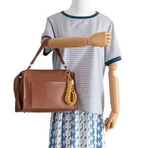 Détail de sac à main en cuir PU marron avec poche avant, fermeture éclair et charm tressé jaune.