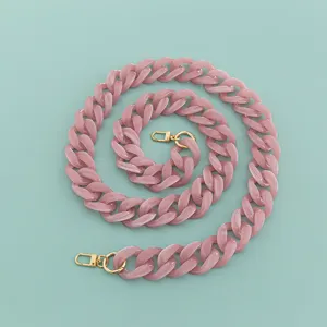 Détail en gros plan de la large bandoulière de sac en résine acrylique rose avec fermoirs dorés.