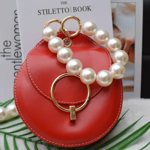 Mini sac rond rouge avec grande poignee en perles et anneau dore, accessoire de mode tendance.
