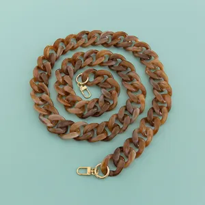 Détail de chaîne de sac en acrylique, sangle en résine marron avec fermoirs métalliques dorés.
