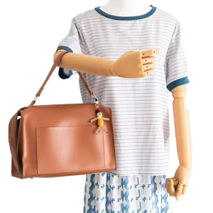 Brown leather handbag detail featuring a quirky handmade beaded doll pendant and metal hardware.