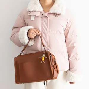 Stylish brown leather handbag paired with unique handmade beaded doll pendant for daily fashion.