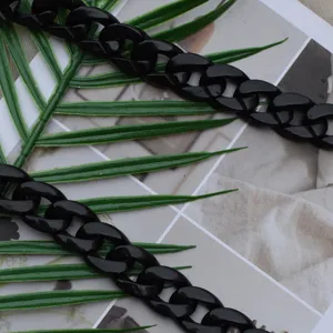 Detailed shot of a black acrylic bag chain, glossy chunky links on green leaves background.