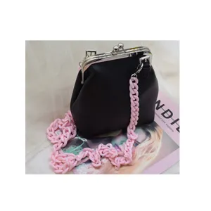 Chic black kiss-lock handbag featuring a bold pink acrylic chain strap. Stylish accessory.