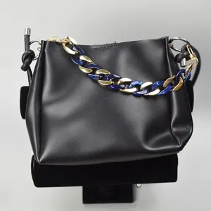 Close-up detail of a stylish black handbag featuring a bold blue and gold chunky chain strap.