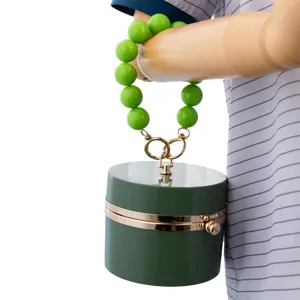 Green cylindrical hard-shell handbag detail with acrylic bead handle and gold metal hardware clasp.