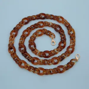 Detailed close-up of brown tortoiseshell acrylic chain with gold clasps for bags or phones.