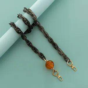 Dettaglio in primo piano della catena per borsa in resina acrilica con perla ambrata e ganci.