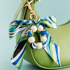 Creative silk scarf wooden bead bow bag charm and keychain shown hanging on a green handbag.