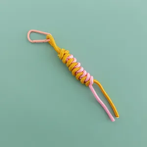 Detail shot of a stylish woven bag charm featuring a pink carabiner and yellow rope.