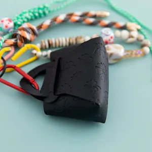 Dettaglio mini borsetta portachiavi in pelle PU nera con motivo quadrifoglio e cordini.