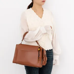Brown leather handbag with elegant pendant charm, stylish structured shoulder bag for daily use.