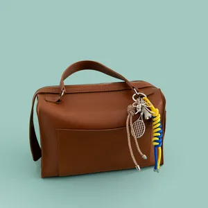 Brown leather handbag with stylish metal tennis racket and colorful rope bag charms.