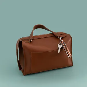 Braune Leder-Box-Tasche mit Reißverschluss, Tragegriff und geflochtenem Schlüsselanhänger.